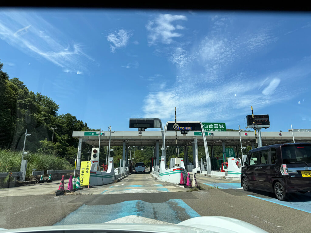 仙台宮城ICから東北自動車道に入ります。青空が広がる背景に、料金所の建物と周囲の緑が映える風景。